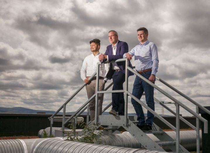 Three Furthr executives stand on a raised metal platform and look into the distance under a cloudy sky.