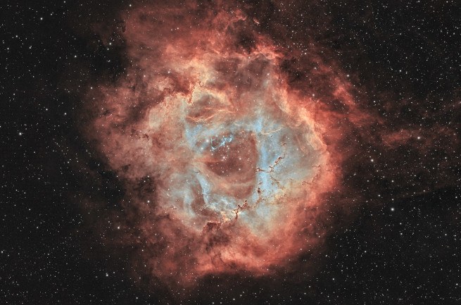 A reddish-brown nebula in space surrounded by darkness and tiny dots of light.