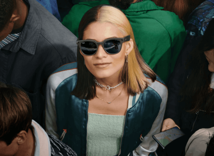 A woman is standing in a crowd wearing the Ray-Ban Stories smart glasses from Meta.