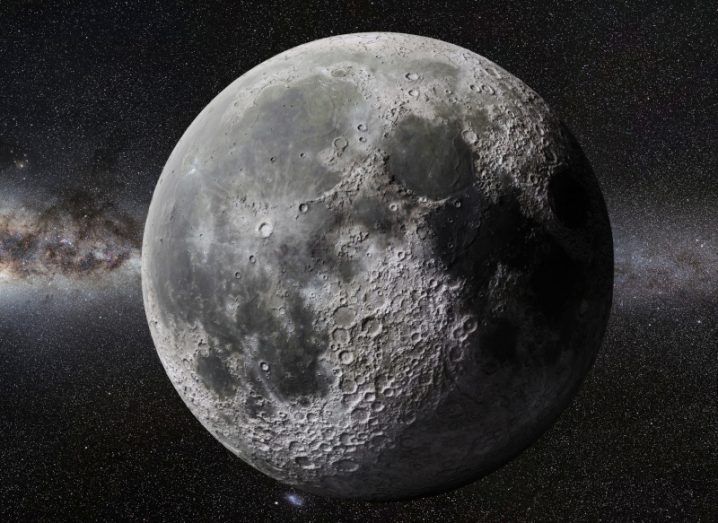 An image of the moon with stars and parts of a galaxy behind it.