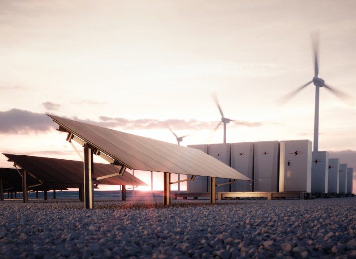 Renewable energy methods, solar panels and wind turbines, outside in a field with a sunset.