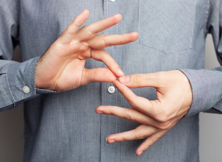 A person wearing a grey shirt making a sign-language symbol with their hands.