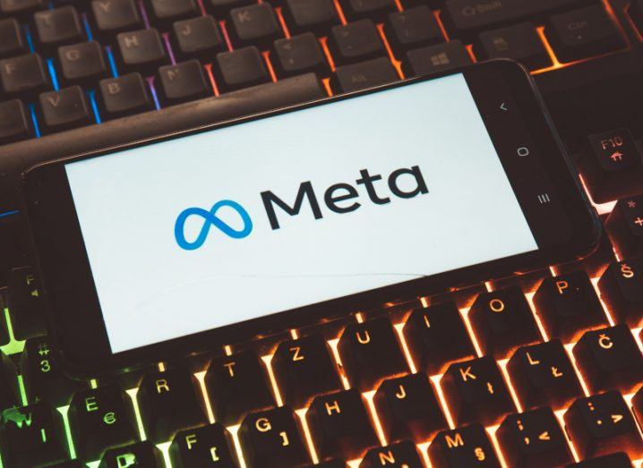 A smartphone resting on a lit up keyboard with Meta logo on it.