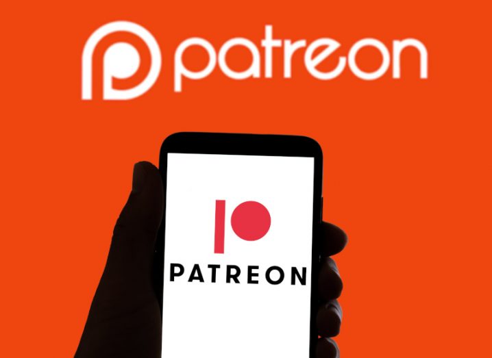 A person's hand holding phone with Patreon app open against red background.