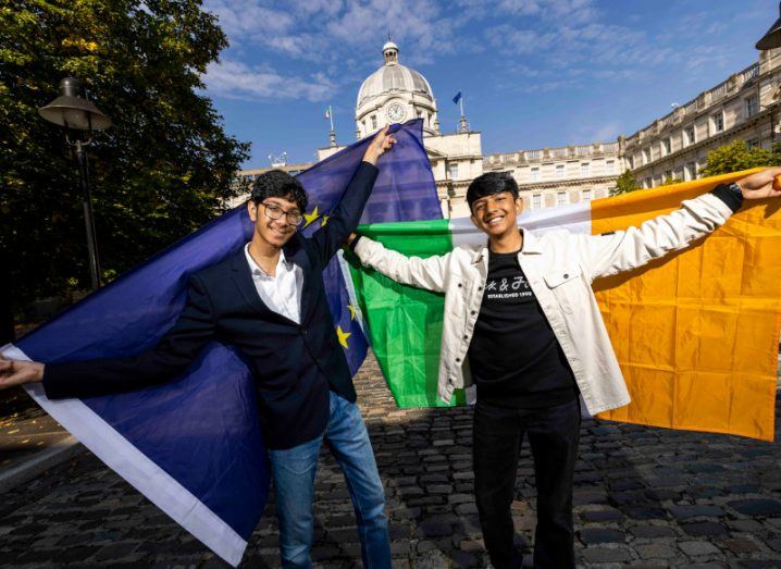 Two students holding an EU flag and an Irish flag behind their backs, with a building, trees and a blue sky in the background. They are Aditya Kumar and Aditya Joshi, winners of the 2022 BT Young Scientist and Technology Exhibition.