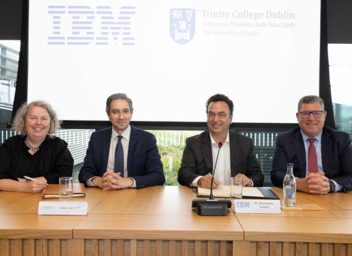 Four people seated at a desk at the signing of a deal between TCD and IBM for research.