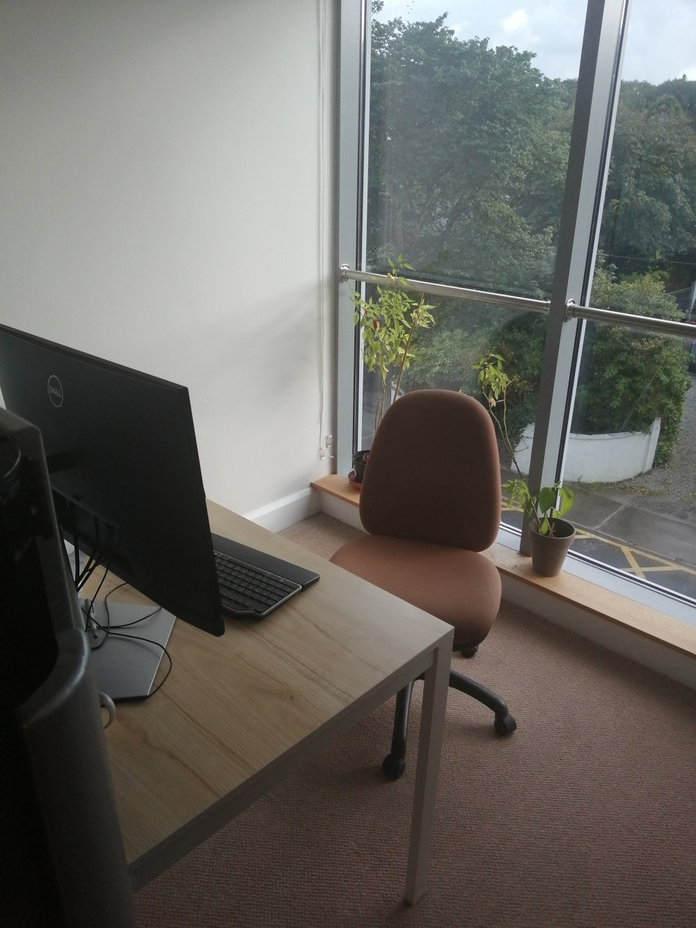 A chair and a desk and monitor positioned against a window offering a view of the road from Soma co-working hub.