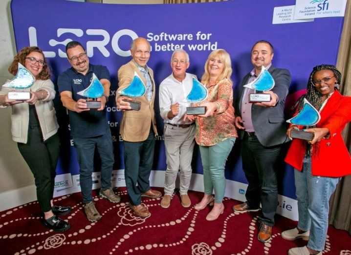Four men and three women standing in front of a purple wall with the Lero logo on it. Six of the people are holding blue awards, from the Lero Director's Prizes ceremony.