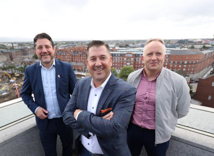 Three men standing on the roof of a building, with city buildings and a grey sky in the background. They are the co-founders of Fexillon and the VP of JE Dunn Construction.