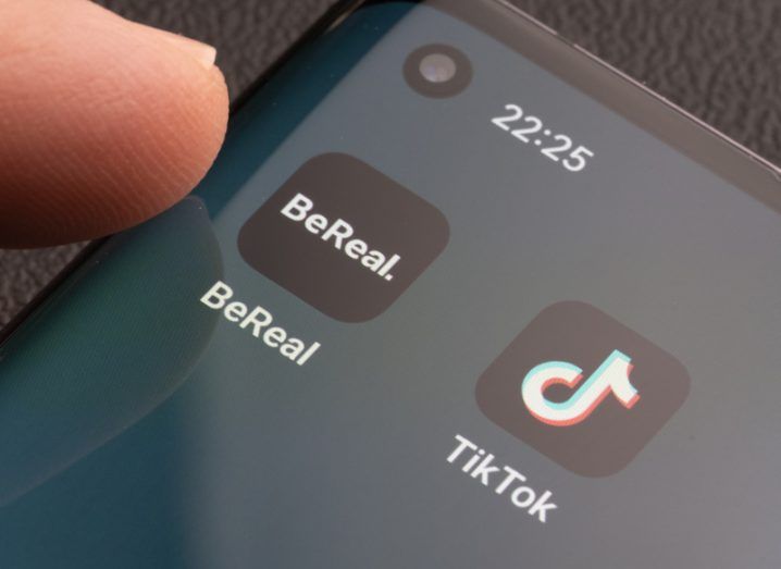 The BeReal and TikTok apps on a smartphone home page with a finger about to tap the screen.