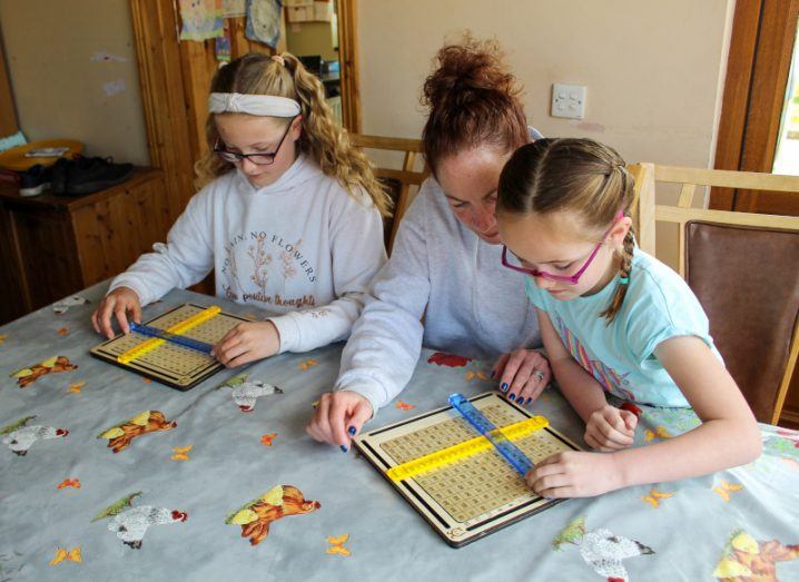 A woman helping two students use the Méadú board for learning maths.