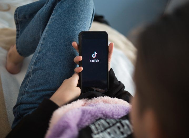 Young child holds a smartphone in their hand with the TikTok app logo displayed on the screen.