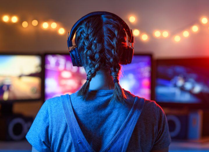 A girl seen from behind wearing a headset and playing video games on a screen.