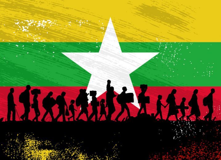 Silhouette of Rohingya refugees walking with the Myanmar flag in the background.