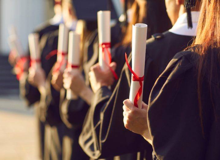 Students wearing graduation robes and holding degree scrolls in their hands.