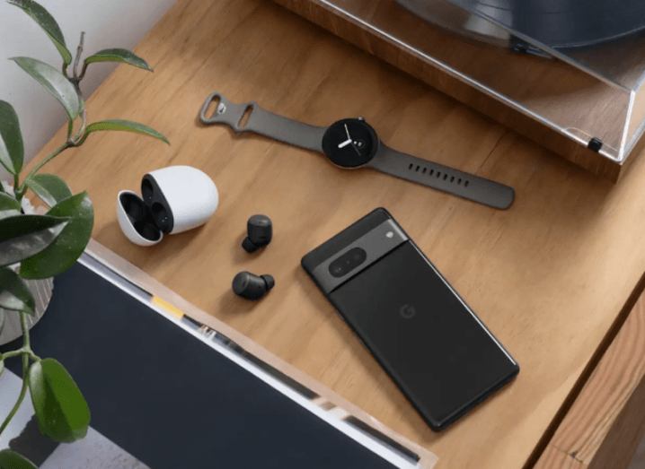 A phone, watch and wireless earbuds on a wooden table. The Google logo is visible on the smartphone.