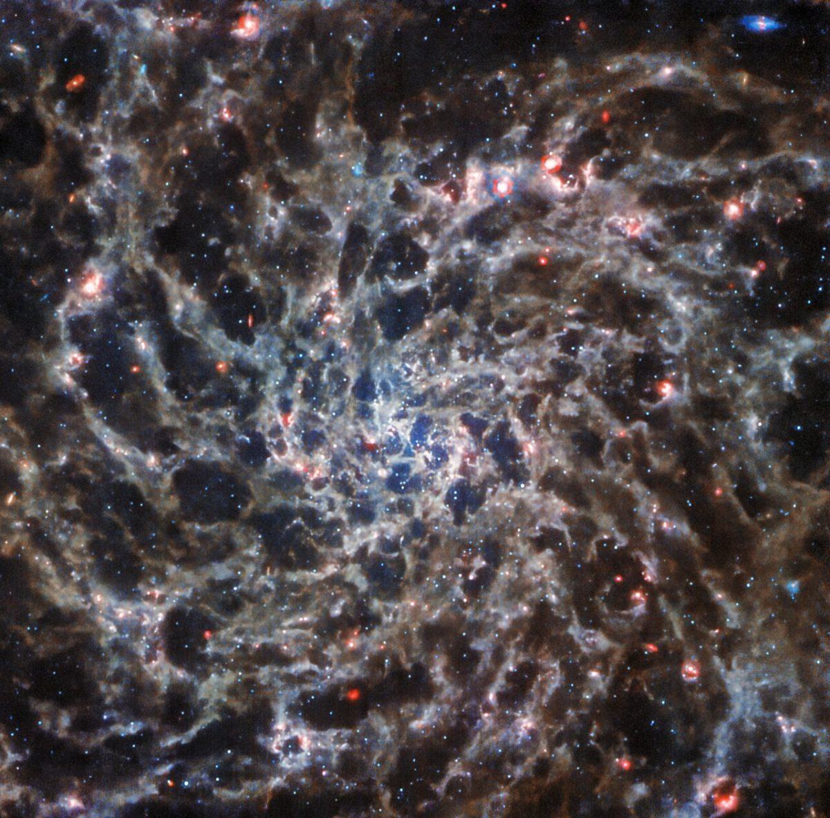 A detailed image of a spiral galaxy, with grey arms and red dots which are distant stars. The image was taken from the James Webb Space Telescope.