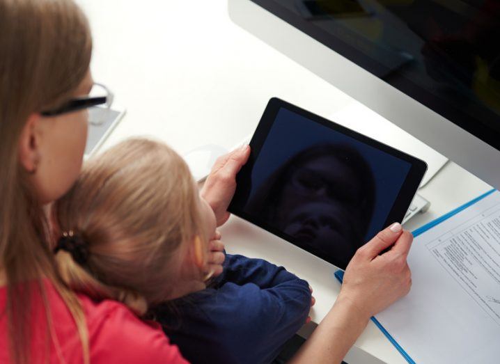 A woman and a child looking at a tablet device being held by the woman, with a monitor screen next to them. Used to represent online safety.