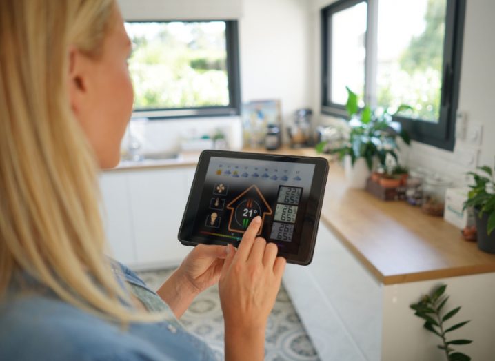 A woman holding a tablet and pressing an app to control the temperature of her home. Used to represent a smart home with IoT devices.