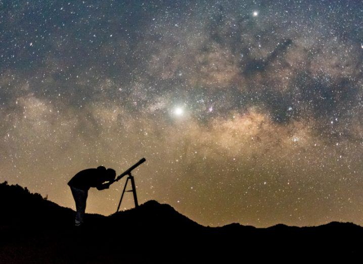Silhouette of an astronomer using a space telescope to observe the night sky.