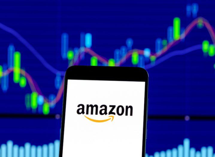 Amazon logo on a smartphone with stock trading image in the background.