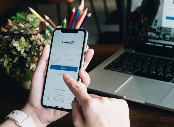 A person is holding up a phone with the LinkedIn login page open on the screen.