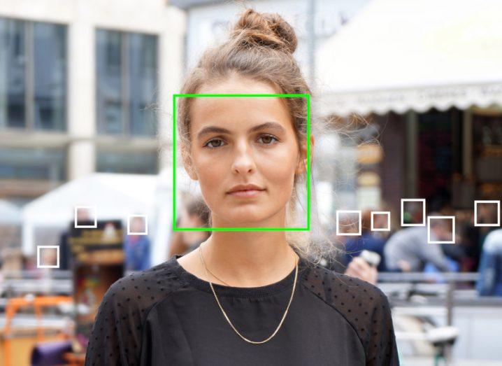 A woman looking at the camera with a green square outline around her face. Other people are in the background with white square outlines around their faces. Used as a concept for biometric and emotion analysis technology.