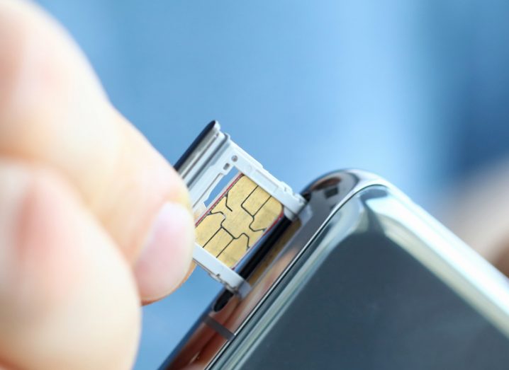 A person holding a SIM card on the side of a smartphone device.