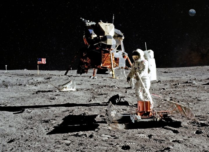 An astronaut explores the moon’s surface next to a lunar landing module.