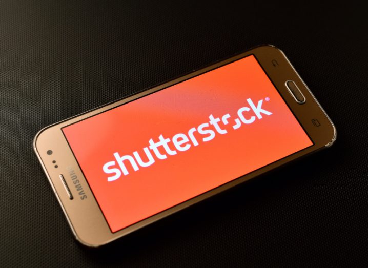 Shutterstock logo in a red background on a smartphone screen, laying face up on a dark background.