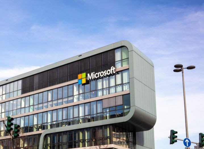 Microsoft logo on the side of a building, with a lampost and traffic lights in front. A blue sky with some white clouds is in the background.