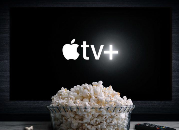 The Apple TV+ logo on the front of a TV screen, with a bowl of popcorn in front of it.