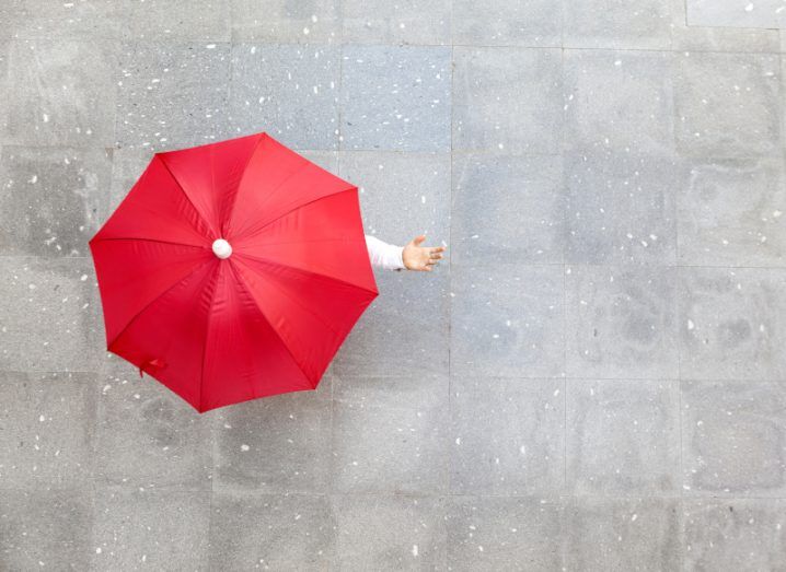 An aerial shot of a person underneath a bright red umbrella, symbolising a business weathering bad conditions.