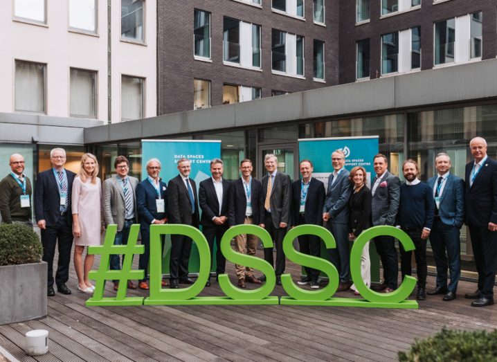 A group of people standing behind a DSSC logo, in front of a building. The DSSC is the Data Spaces Support Centre.