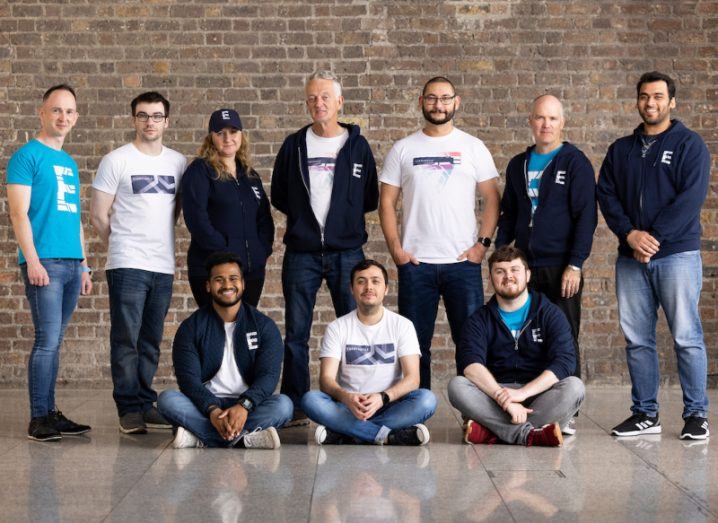 A group of people in Everyangle-branded hats and T-shirts stand in front of a red-brick wall.