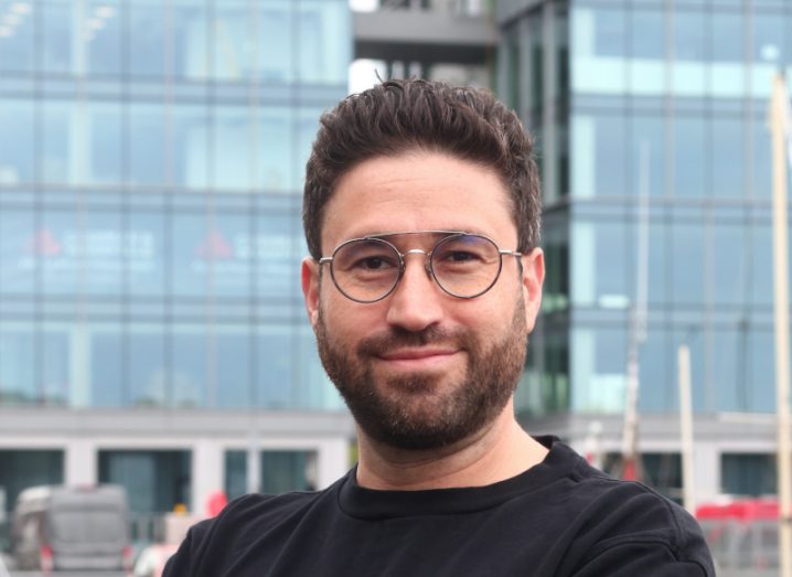 A man with dark hair and glasses smiles at the camera while standing in front of a large glass building. He is Josh Builder, CTO of Signify Health.