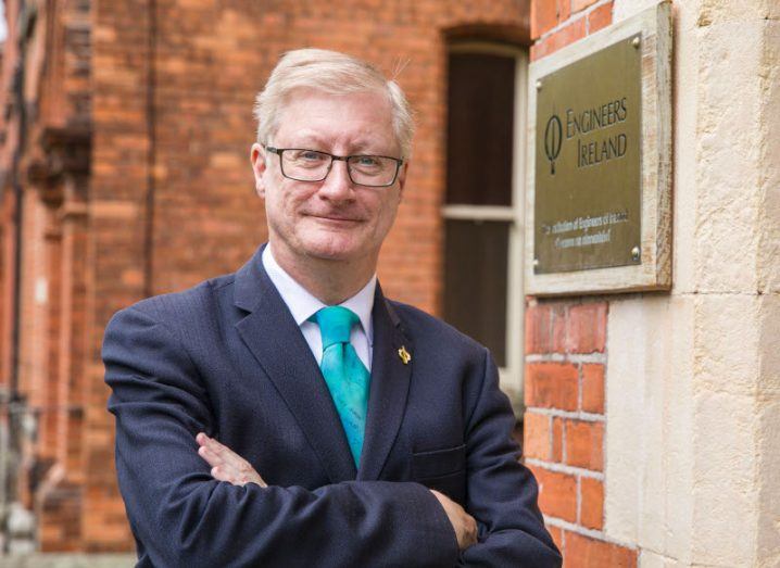 Damien Owens, director general, Engineers Ireland standing outside a red brick building with an Engineers Ireland gold plaque on the wall.