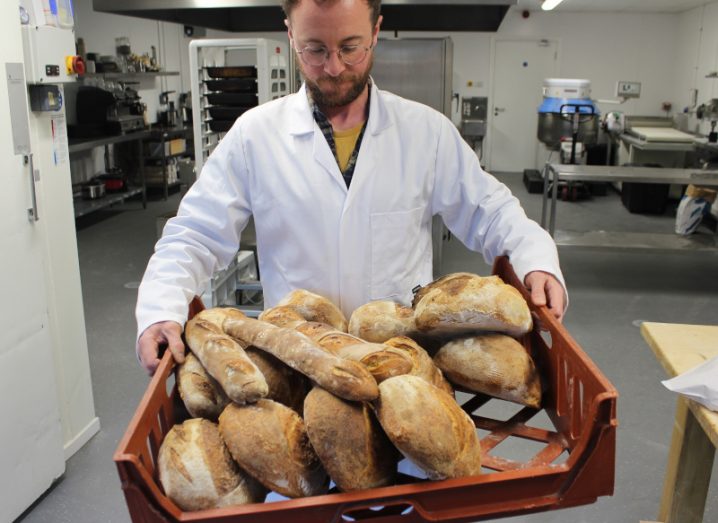 A man in a white coat holding a basket full of bread. He is Dr Tony Callaghan, co-founder of Niskus Biotech.