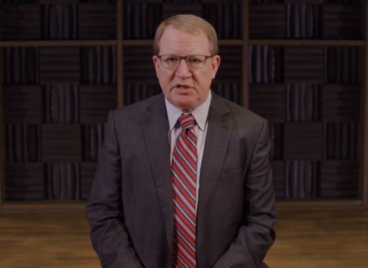 A man wearing a suit and a tie in front of a brown wooden wall with a wooden floor visible behind him. He is Paul Wellener of Deloitte.