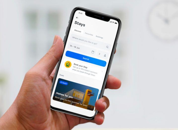 A hand holding a smartphone with Revolut stays open on it and options to book a holiday home.