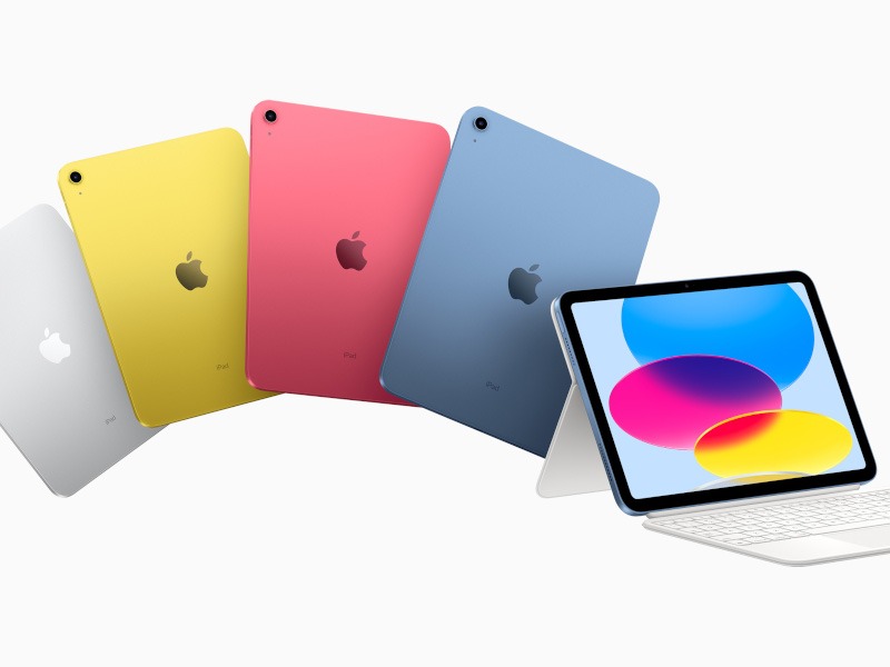 Four iPads in blue, pink, yellow and silver next to each other. Another iPad is attached to a keyboard with the screen on.