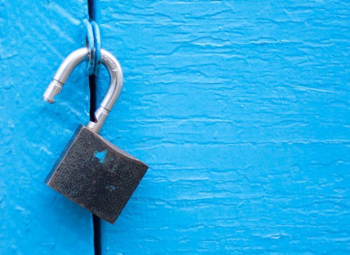 Photo of an unlocked padlock hanging from a bright blue door.