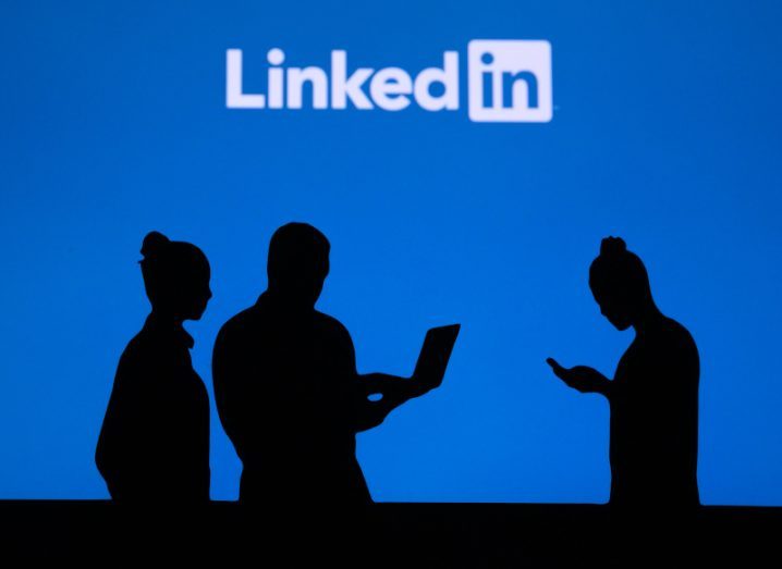 Silhouettes of people standing in front of the LinkedIn logo.