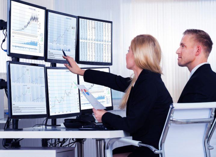 Two office workers analysing AI data on multiple computer screens.