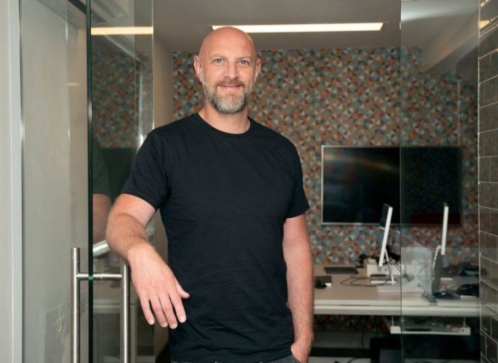Ekco CEO Eoin Blacklock wearing a black t-shirt and trousers in an indoor office space.