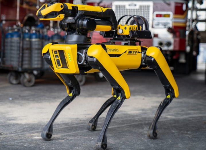 A yellow Boston Dynamics general purpose mobile robot called Spot, standing in a warehouse.