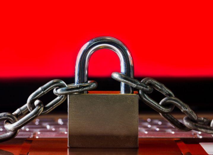 A lock with chains resting on a laptop keyboard with a red screen in the background. Used to represent ransomware.
