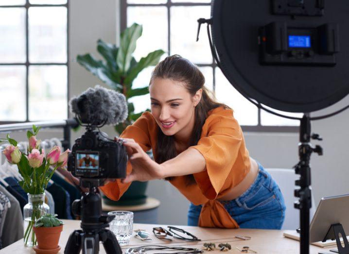 Woman content creator setting up a camera in a modern office environment with camera equipment all around.