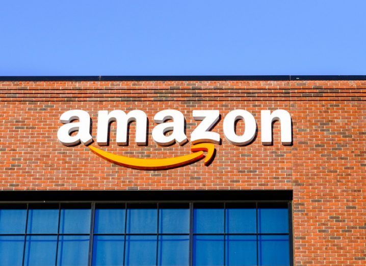 Amazon logo on the top of a brown coloured building, with a clear blue sky above and windows below it.