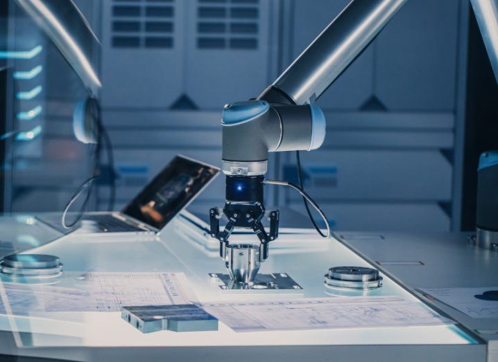 A robot arm moving to grab a metal object on a table in a high tech office setting.